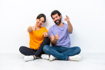 Fototapeta na wymiar Young caucasian couple sitting on the floor isolated on white background points finger at you with a confident expression