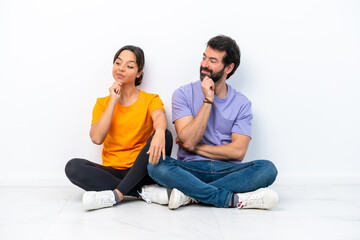 Fototapeta na wymiar Young caucasian couple sitting on the floor isolated on white background looking to the side