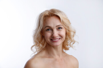 Fototapeta premium Studio portrait of sensual adult woman with clean smooth face skin, smiling over isolated white background. Happy middle aged female with wavy blonde hair and naked shoulders. Close up, copy space.