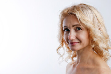 Studio portrait of sensual adult woman with clean smooth face skin, smiling over isolated white background. Happy middle aged female with wavy blonde hair and naked shoulders. Close up, copy space.