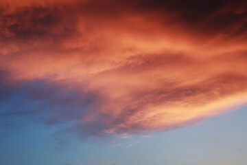 Naklejka na ściany i meble Dramatic sunset landscape with puffy clouds lit by orange setting sun and blue sky.