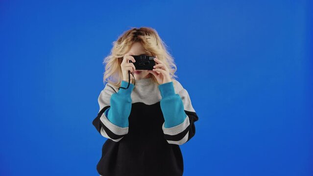 Teenage caucasian blonde girl taking picture with film camera. Blue screen studio background