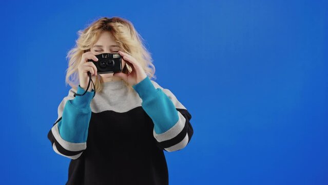 Teenage caucasian blonde girl taking photo with film camera. Blue screen studio background