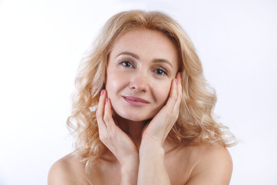 Studio portrait of sensual adult woman with clean smooth skin touching her face over isolated white background. Middle aged female with wavy blonde hair and naked shoulders. Close up, copy space.