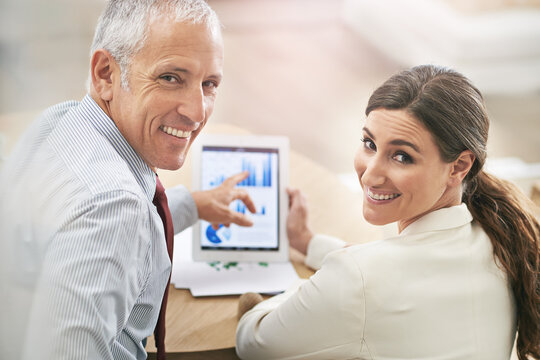 Our Business Is Trending Upwards. Portrait Of Two Coworkers Sitting At A Table Using A Digital Tablet.