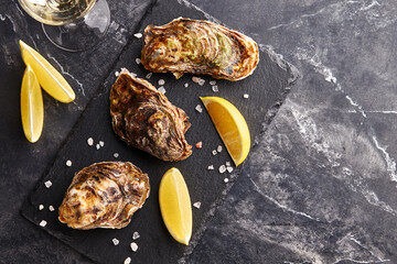 Fresh closed oysters with lemon on slate plate