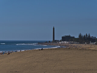 Fototapeta premium Aerial view over crowded beach Playa de Maspalomas with sand dune in front and lighthouse Faro de Maspalomas in the south of Gran Canaria, Spain.