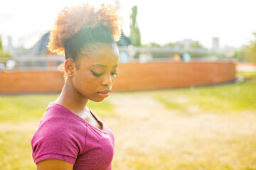 Sad african american woman with curly hair looking down in park outdoors