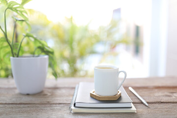 Tea cup and brown kraft notebooks and Window Monstera obliqua leaf plant