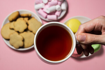 Obraz na płótnie Canvas The hand holds a cup of tea on the background of sweets. Cup of tea on a pink background. Sweet breakfast