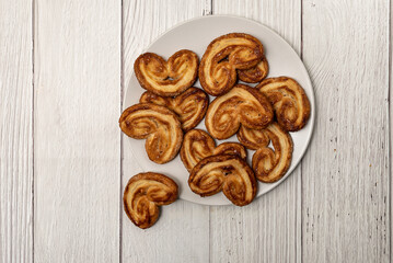 Palmier puff pastry biscuits in white plate on a white painted wooden table