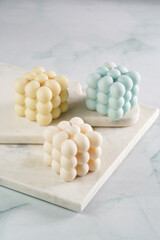 Three bubble candles - off-white, beige-colored and blue - on marble board on pale blue surface