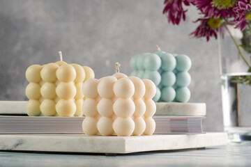 Three bubble candles - off-white, beige-colored and blue - on marble board on pale blue surface