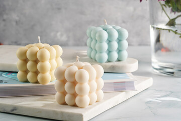 Three bubble candles - off-white, beige-colored and blue - on marble board on pale blue surface