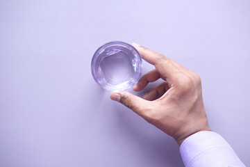 hand holding a glass of water on purple background 