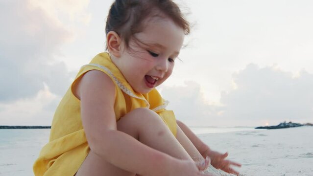 Happy toddler girl plays with sand on the tropical beach in Maldives
