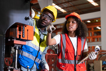 African mechanical engineer team, wearing safety equipment. While doing machine maintenance and safety control while work inside of factory area. With blurred background of heavy machine.