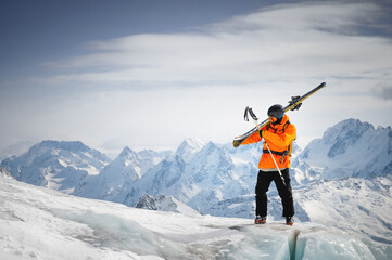 Portrait of a young skier with skis on his shoulder. It stands high in the mountains on a glacier...