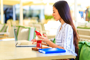 Image of happy asian woman using laptop while sitting at cafe