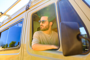 Young man driving house on wheels truck by mountains road in summer day