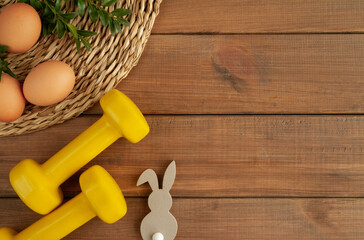 Two heavy dumbbells, decorative Easter bunny, eggs and boxwood branches. Healthy fitness lifestyle...