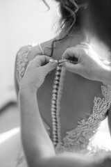 Dettaglio in bianco e nero di due mani in cui vengono abbottonati i bottoni di un abito da sposa 
