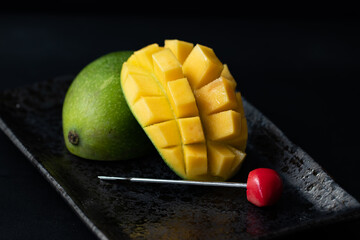 Fresh mango fruit on black plate on black background.