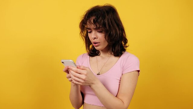 Beautiful woman reading sad news on her phone. Attractive young girl on yellow background.