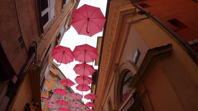 Grasse, France, October 3, 2021: TIMEWARP Suspended pink umbrellas in the historic center of Grasse, celebrating the Rose Expo. Elements of architecture of Grasse with colored umbrellas between houses