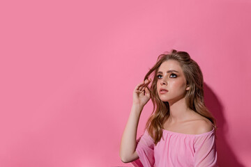 Photo portrait of a teenage woman with blond wavy hair on a pastel pink color background. She's looking up, copyspace