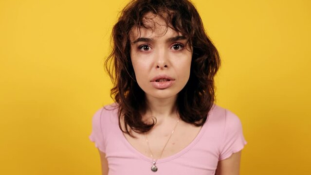 Girl looks at something and can't understand what it is. Attractive young woman on yellow background.