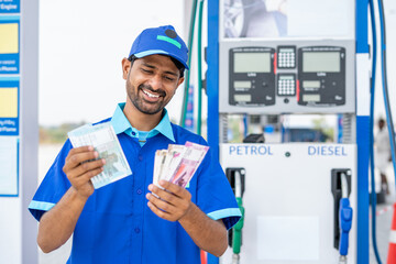 Smiling gas filling station attendant counting money at petrol pump - concept of business profit,...