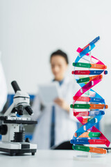 selective focus of dna model near microscope and geneticist on blurred background.