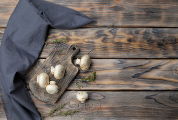 Raw mushrooms on a wooden plank. Dried rosemary is scattered on the table. Dark wooden background,...