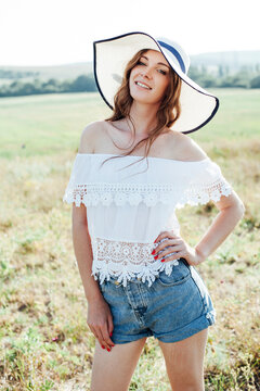 a beautiful woman in a hat in a field at sunset