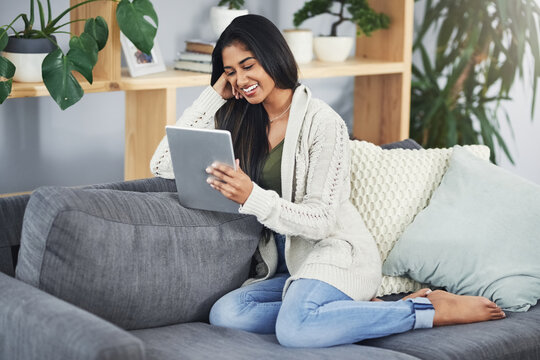 These modern-day sites can sure make ones day. Shot of a happy young woman using her digital tablet while relaxing on her couch at home.