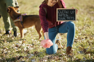 Unrecognizable pet owner holds chalkboard with 'clean up after your pets' message in park.