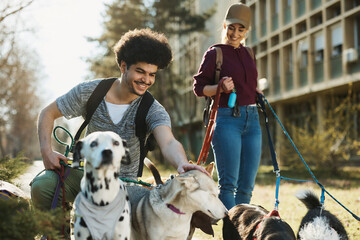 Happy pet sitters enjoy with group of dogs during a walk in park.