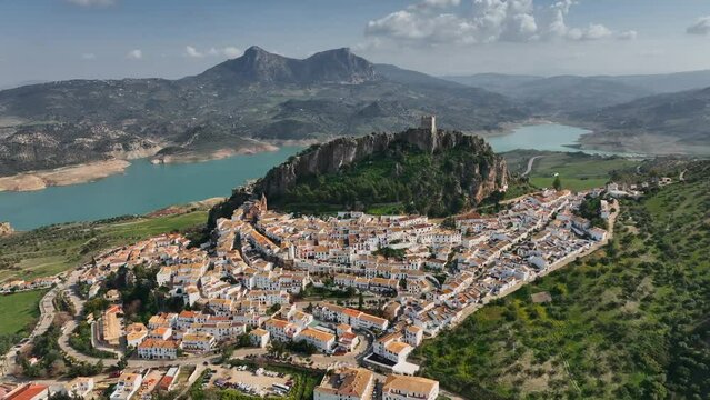 Flying over the orange roofs of the town, fortress on the mountain and the view of the river in Zahara de la sierra.