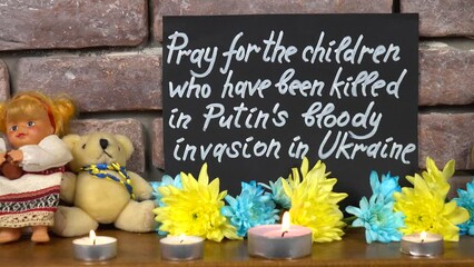 The appeal to pray for the children who have been killed in Putin's bloody invasion in Ukraine written on a black paper, toys, burning candles, flowers are placed near a brick wall.