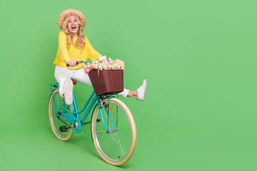 Photo of funny funky woman wear yellow sweater cap riding bike empty space isolated green color...