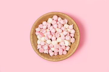 Merengues rosas y blancos dentro de un cuenco de madera sobre un fondo rosa pastel liso y aislado. Vista superior. Copy space
