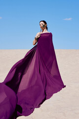 Amazing beautiful brunette woman with the Peacock feather in purple fabric in the desert. Oriental, Indian, fashion, style concept