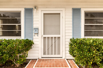 White front door with a screen door. A brick path leads to an entrance.