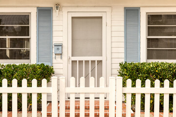 White front door with a screen door surrounded by a white picket fence..