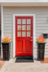 Red front door with black doormat, black pots filled with flowers.