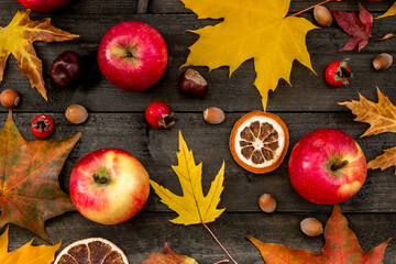 Autumn background maple leaves, apples, rose hips, nuts, chestnuts, dried oranges on a wooden table