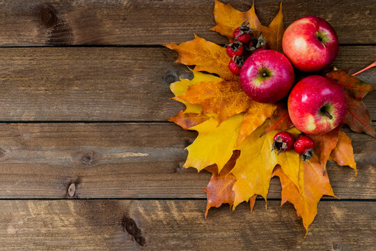 Autumn composition of apples, maple leaves and rose hips on a wooden table