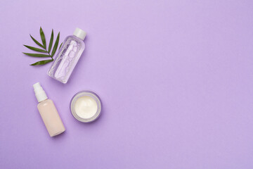 Facial tonic and cream with green leaves on color background, top view