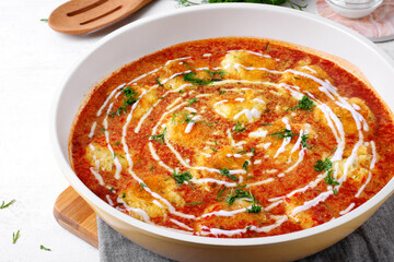 Malai kofta topped with yogurt and fresh herbs. Hot meal with potato and paneer cheese balls in tomato sauce served in the pan. Indian cuisine